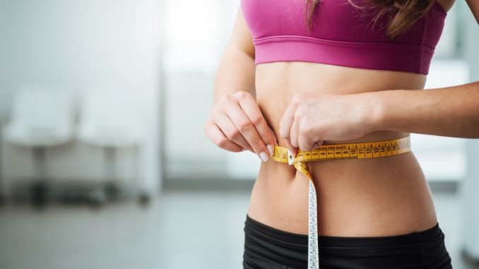 Slim young woman measuring her thin waist with a tape measure, close up